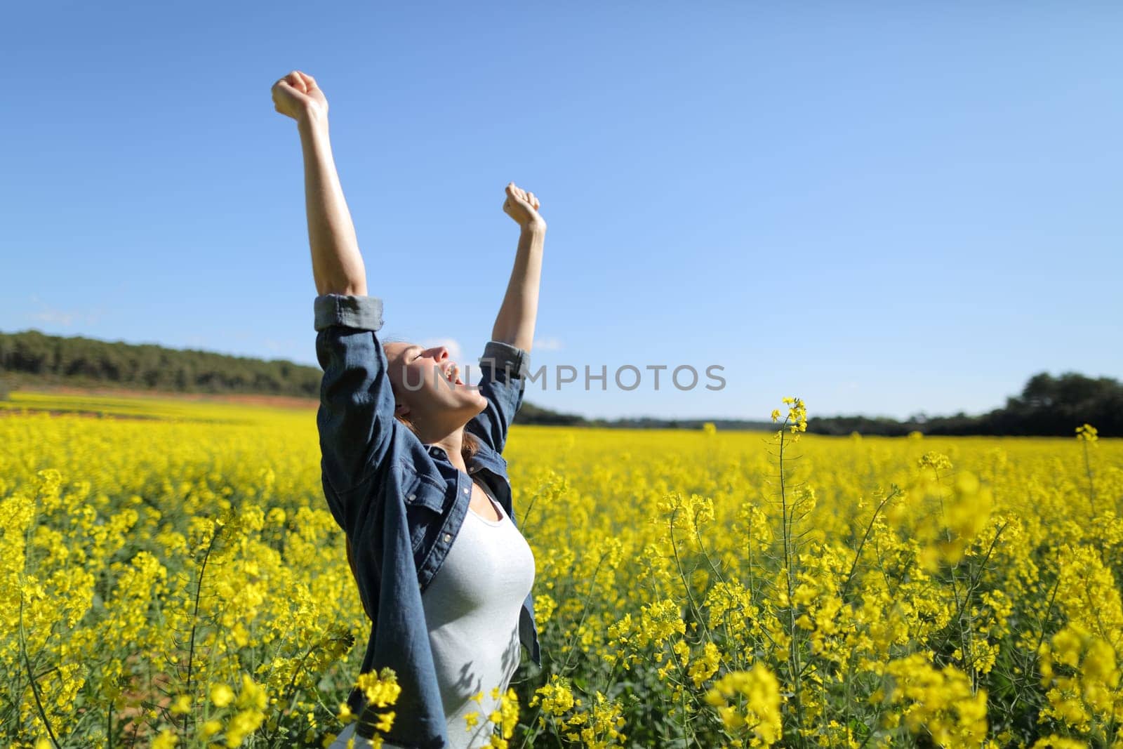 Excited female raising arms celebrating spring in a field
