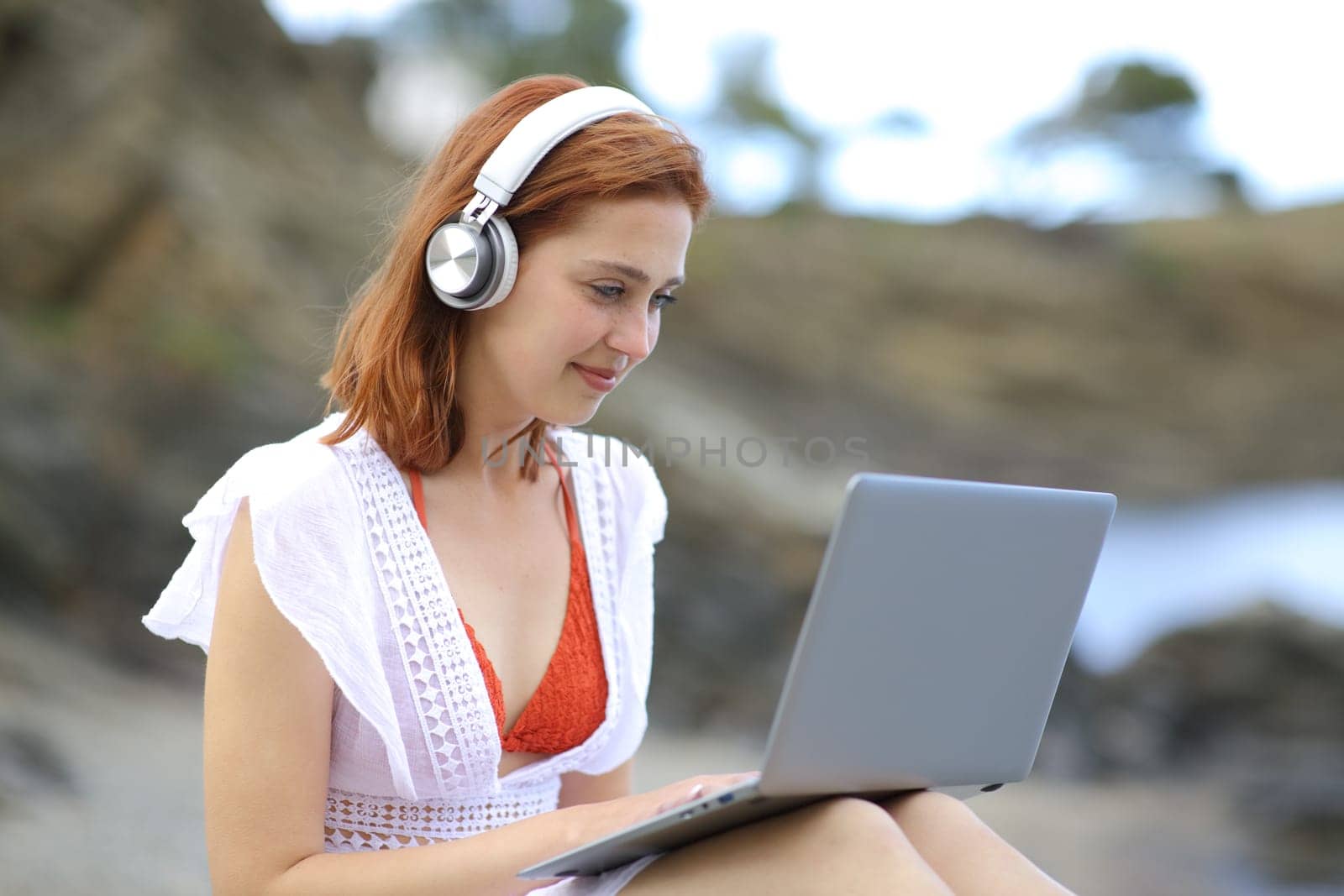Tourist using a laptop with headphones on the beach