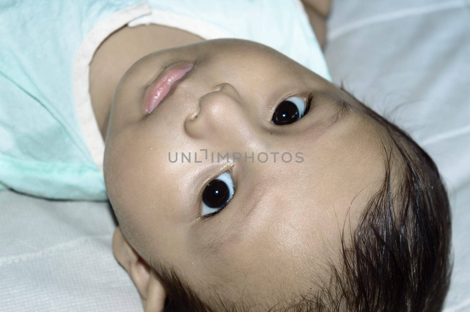 Close up face of cute newborn baby boy upside down and Looking at camera. Four month old Sweet little infant toddler Closeup portrait. Indian ethnicity. Front view. Child Health care background.