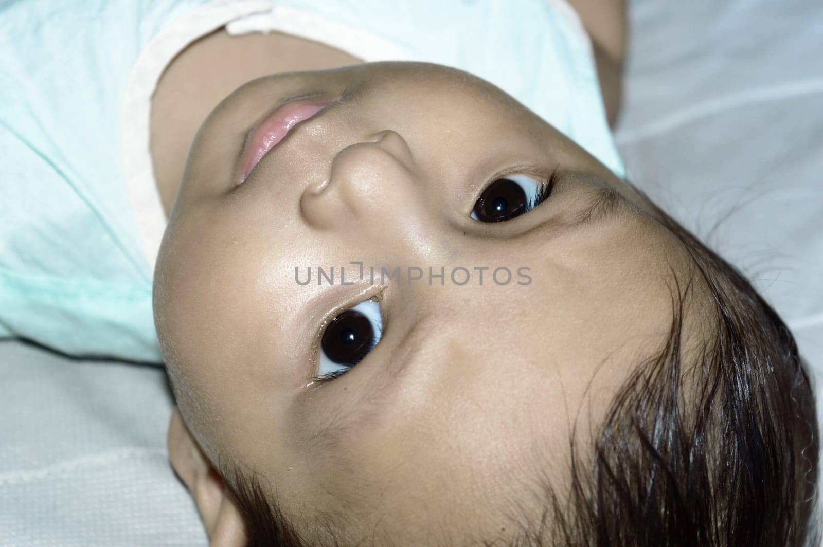 Close up face of cute newborn baby boy upside down and Looking at camera. Four month old Sweet little infant toddler Closeup portrait. Indian ethnicity. Front view. Child Health care background.
