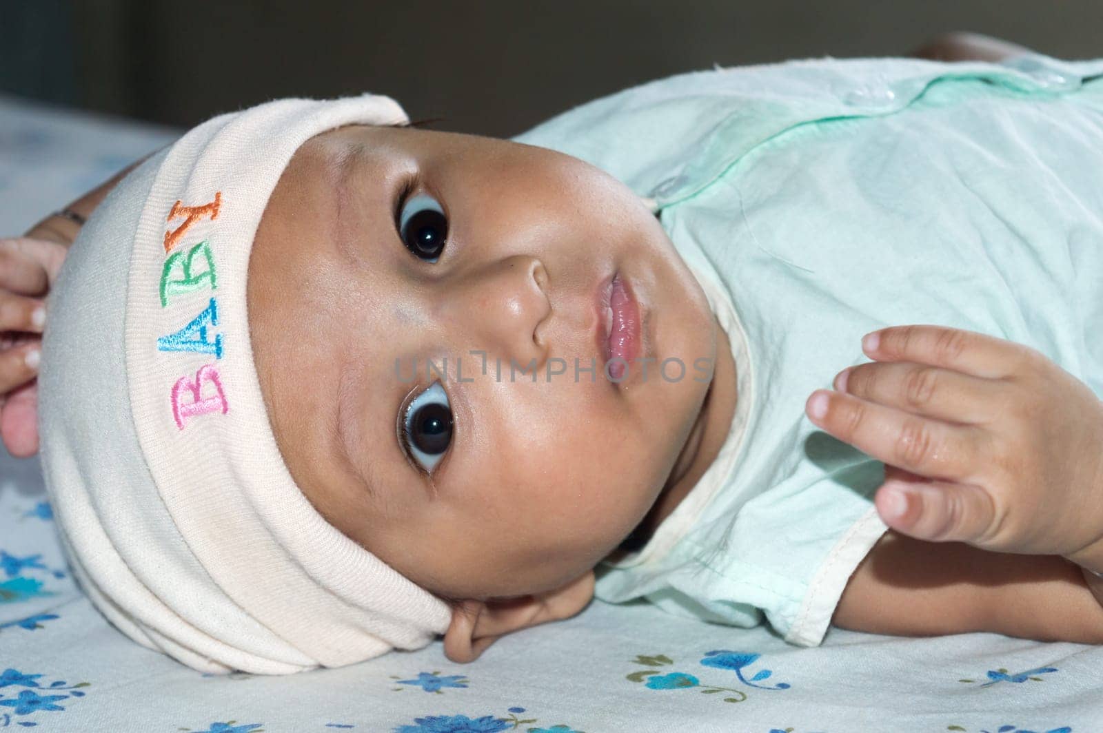 Upside down Closeup cute face of newborn baby boy lying on bed and Looking at camera. Sweet little infant toddler Closeup portrait. Indian ethnicity. Front view. Child Health care medical background.