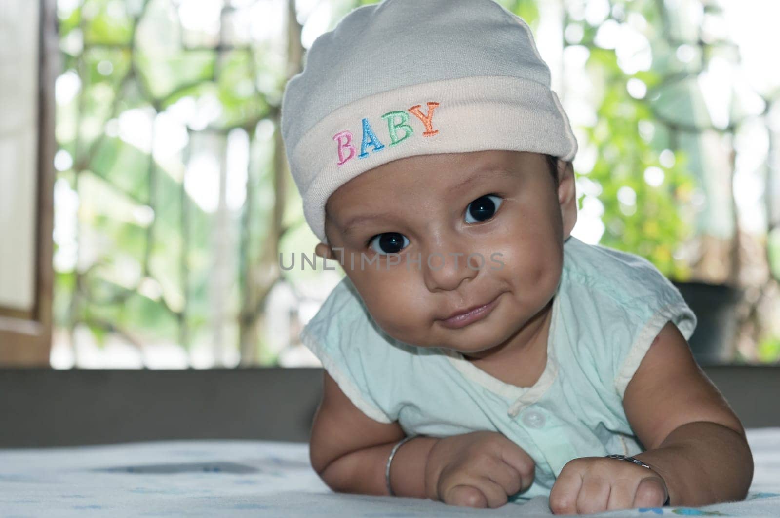 Cute baby lifting head. Closeup portrait. Happy baby boy looking and smiling at camera. Health care medical background. Sweet little infant toddler. Indian ethnicity. Developmental milestone for baby.