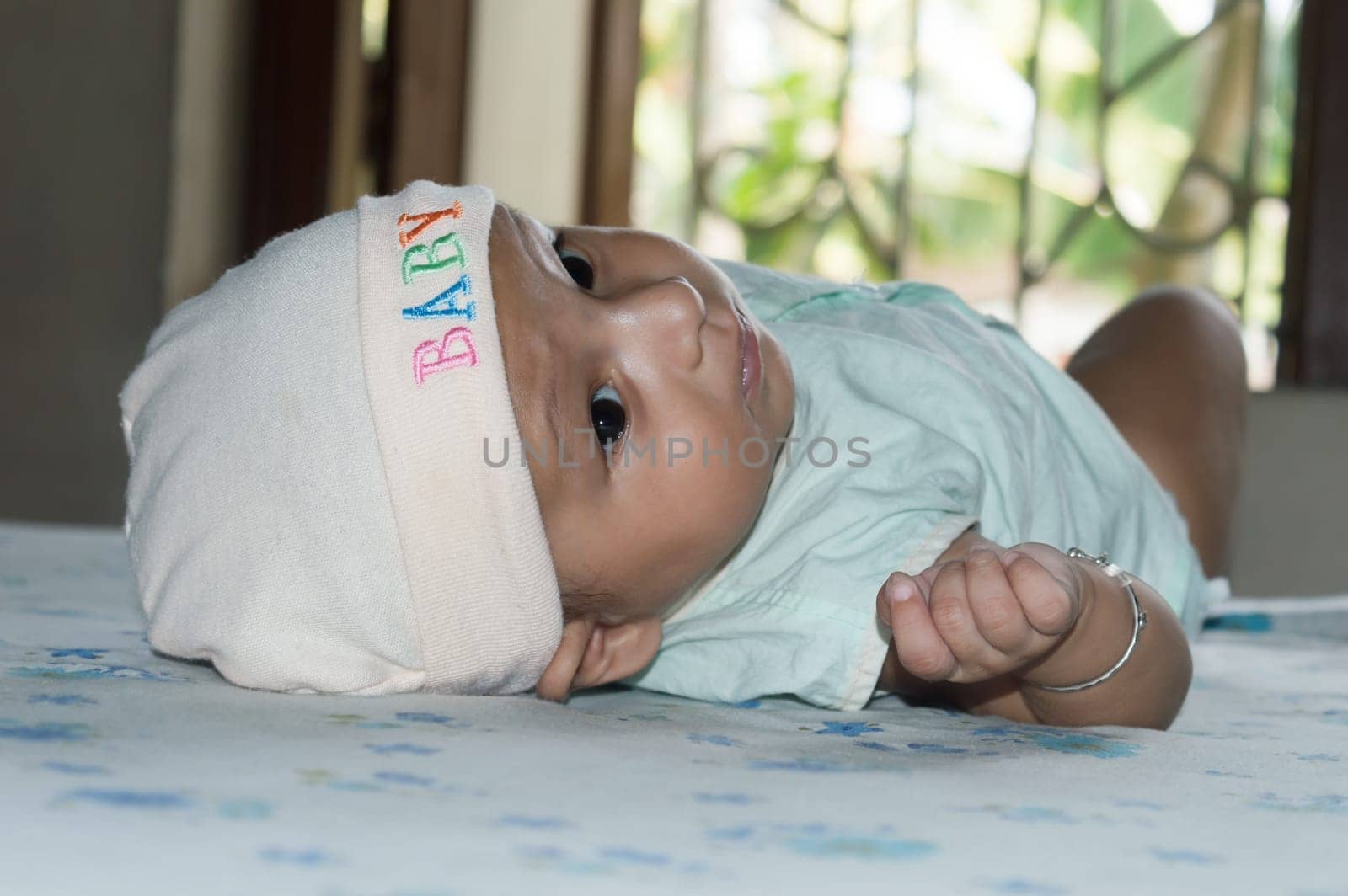 Upside down Closeup cute face of newborn baby boy lying on bed and Looking at camera. Sweet little infant toddler Closeup portrait. Indian ethnicity. Front view. Child Health care medical background.
