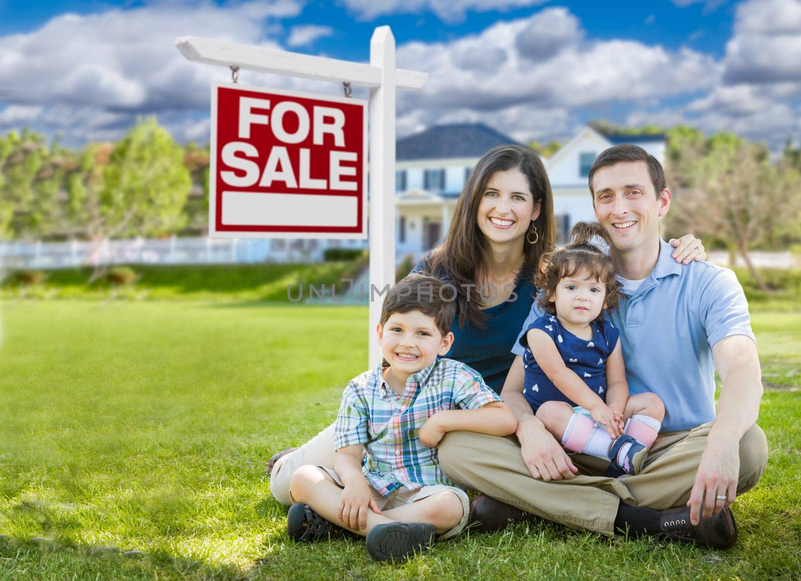 Young Family With Children In Front of Custom Home and For Sale Real Estate Sign.