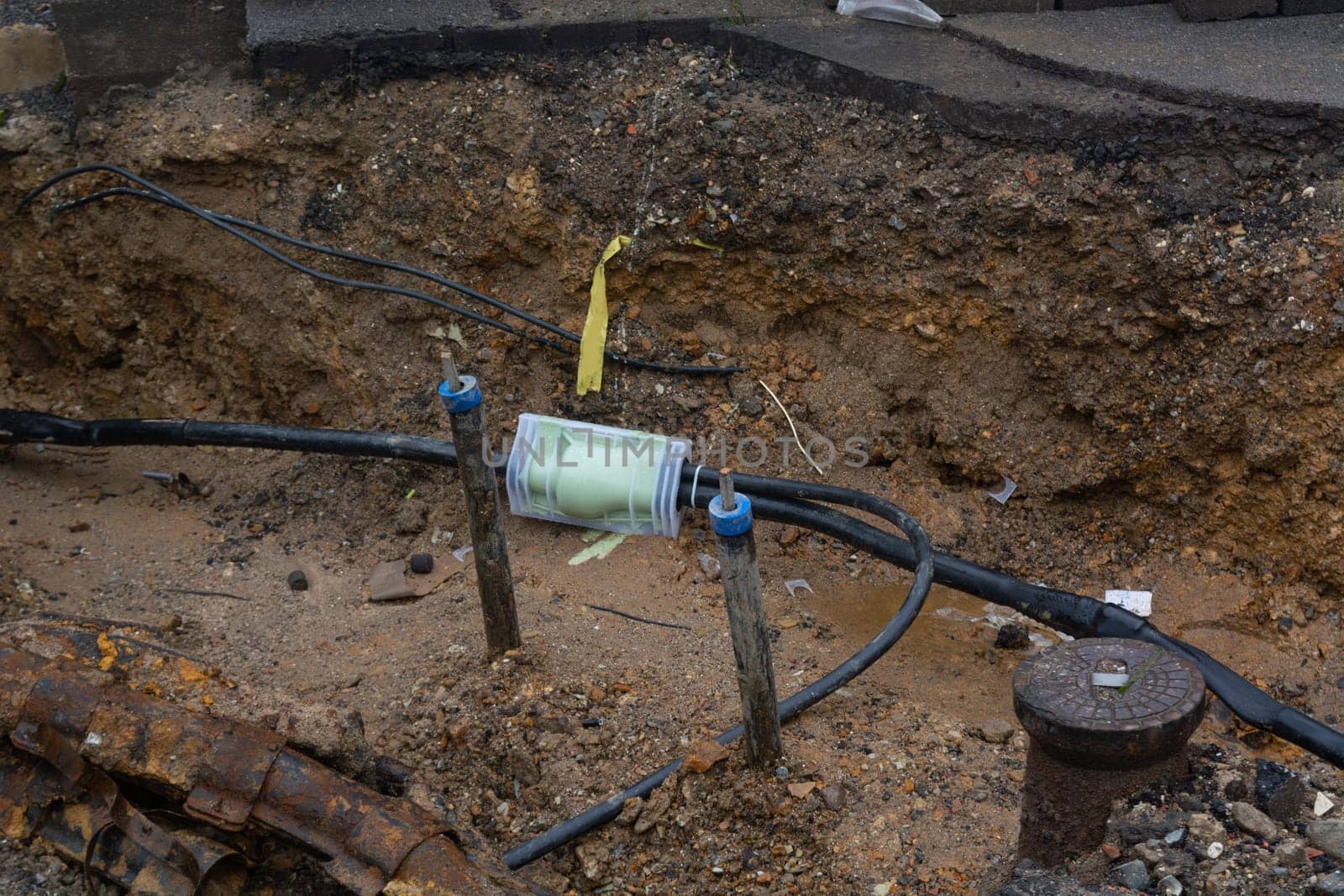 Dug up sidewalk revealing wires in protective tubes. Building of electric lines or telecommunication cables, construction of optical network connection. Excavation and maintenance