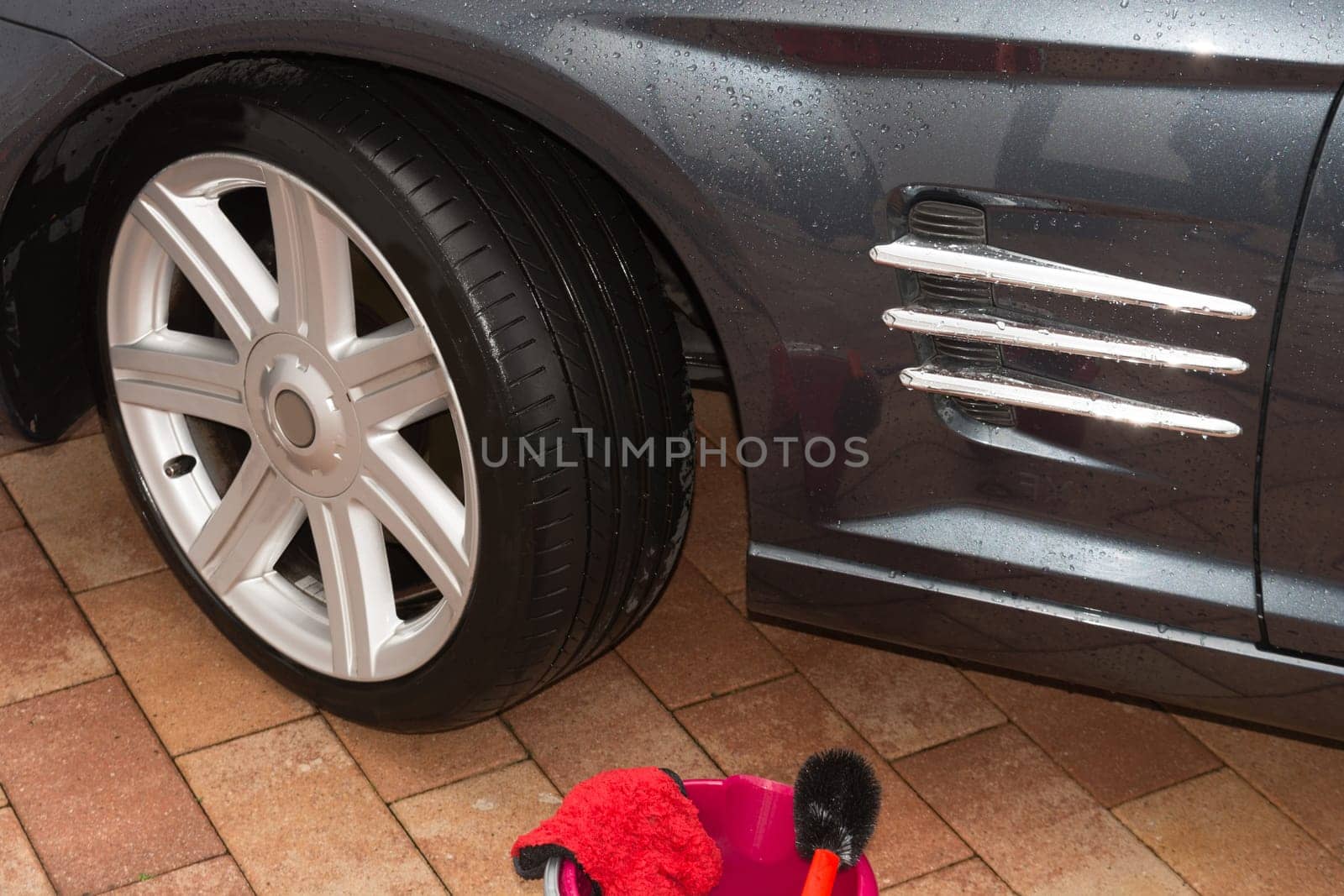 Car rims cleaning, car detailing wash concept. Cropped close up photo of male hand in black rubber glove with blue microfiber cloth washing car alloy wheel at car wash service
