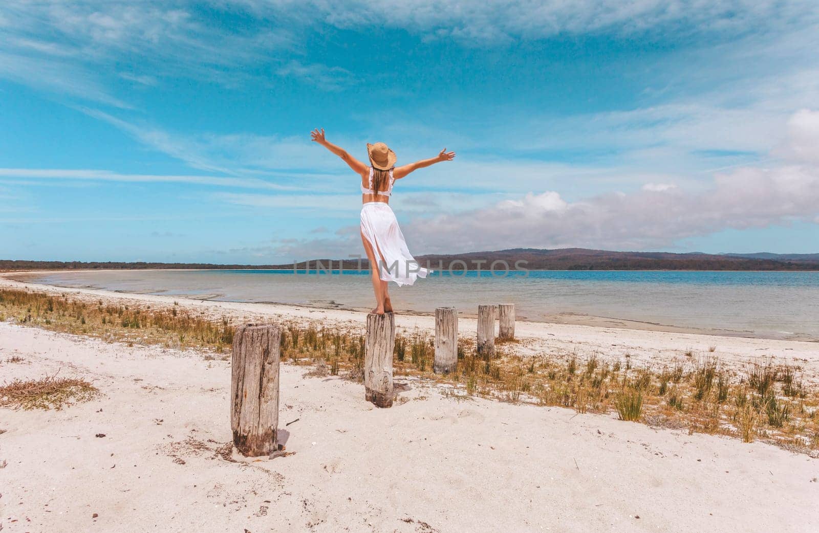 A woman throws her arms up over her head in sheer joy and zest for life on vacation by a beautiful beach setting in Australia