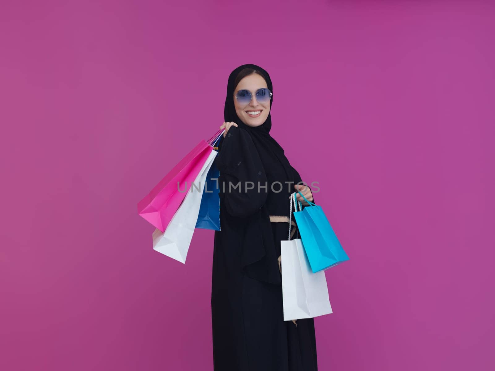 Happy muslim girl posing with shopping bags. Arabic woman wearing traditional black clothes and sunglasses representing rich and luxurious lifestyle