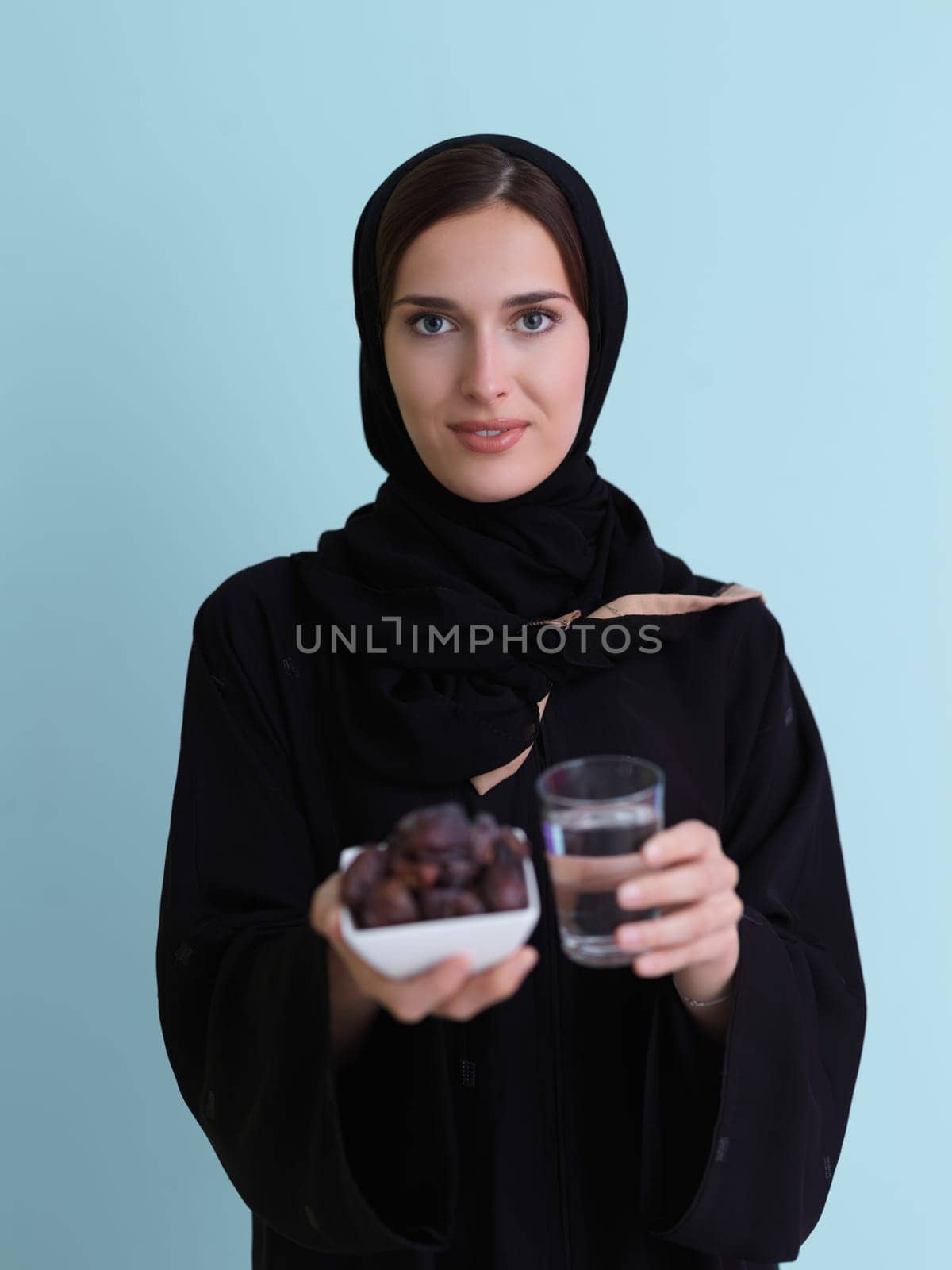Modern muslim woman in abaya holding a date fruit and glass of water in front of her. Concept celebration of iftar time, end of fasting, in ramadan holy month