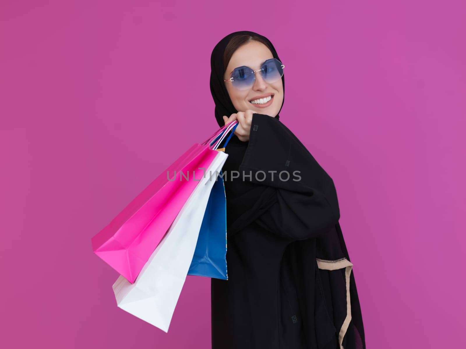 Happy muslim girl posing with shopping bags. Arabic woman wearing traditional black clothes and sunglasses representing rich and luxurious lifestyle