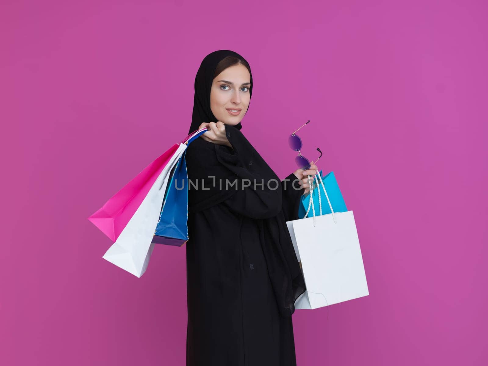 Happy muslim girl posing with shopping bags. Arabic woman wearing traditional black clothes and sunglasses representing rich and luxurious lifestyle