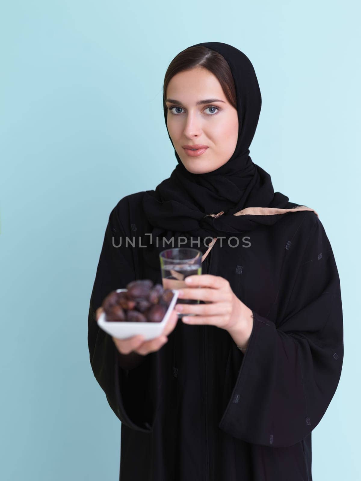 Modern muslim woman in abaya holding a date fruit and glass of water in front of her. Concept celebration of iftar time, end of fasting, in ramadan holy month