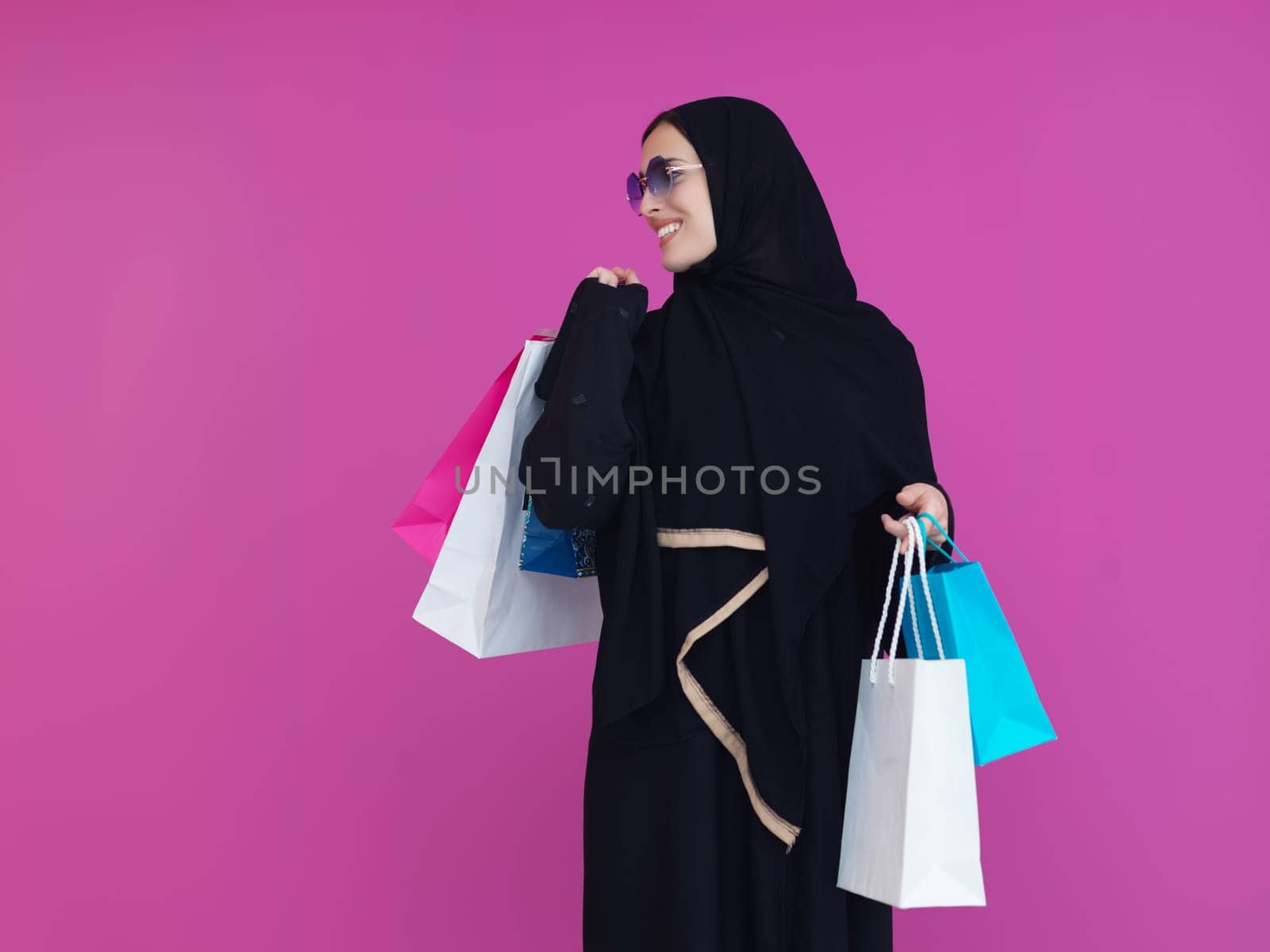 Happy muslim girl posing with shopping bags. Arabic woman wearing traditional black clothes and sunglasses representing rich and luxurious lifestyle