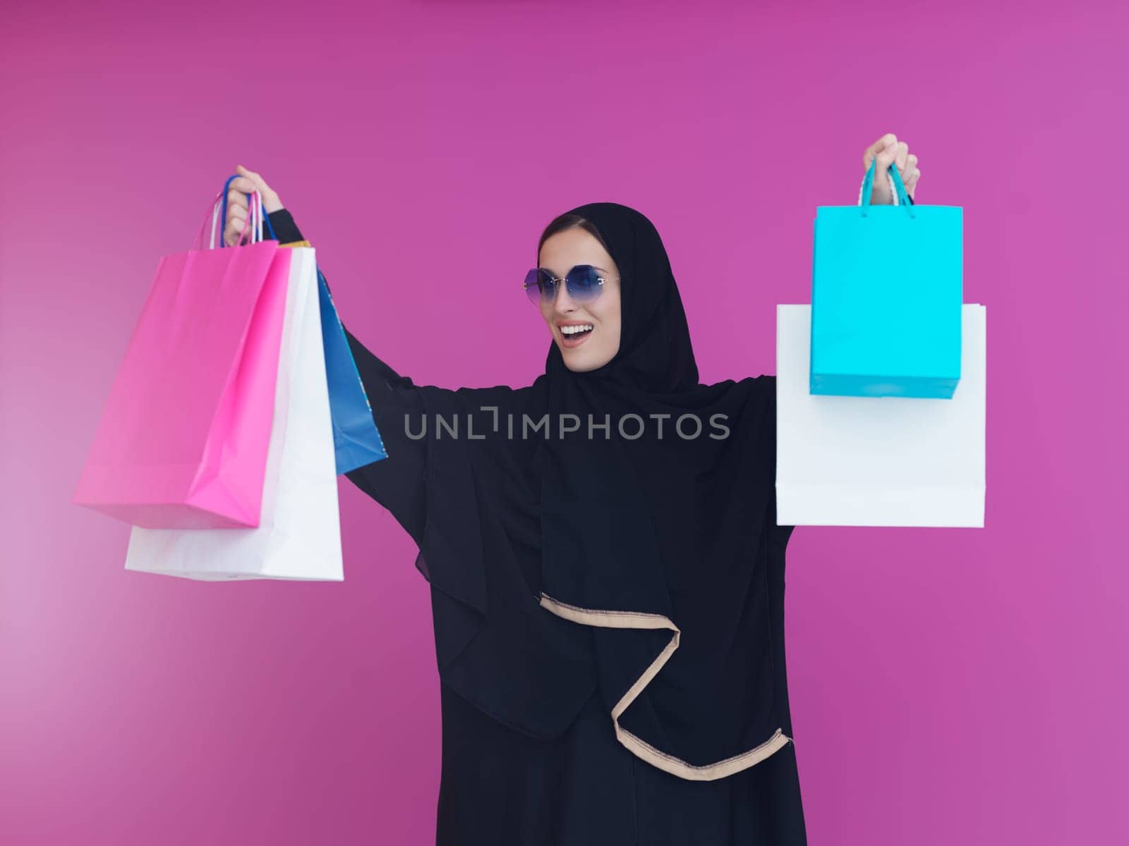 Happy muslim girl posing with shopping bags. Arabic woman wearing traditional black clothes and sunglasses representing rich and luxurious lifestyle