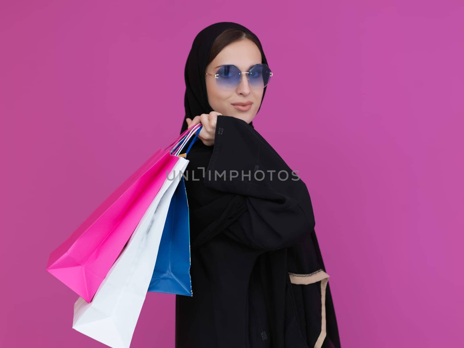 Happy muslim girl posing with shopping bags. Arabic woman wearing traditional black clothes and sunglasses representing rich and luxurious lifestyle