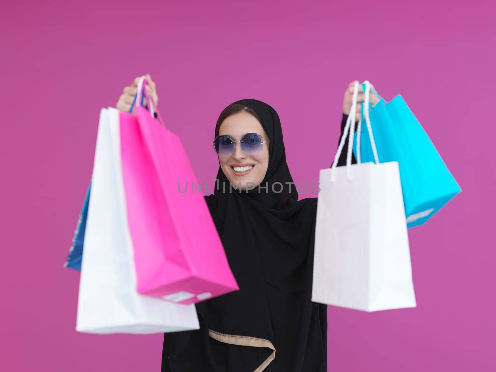 Happy muslim girl posing with shopping bags. Arabic woman wearing traditional black clothes and sunglasses representing rich and luxurious lifestyle