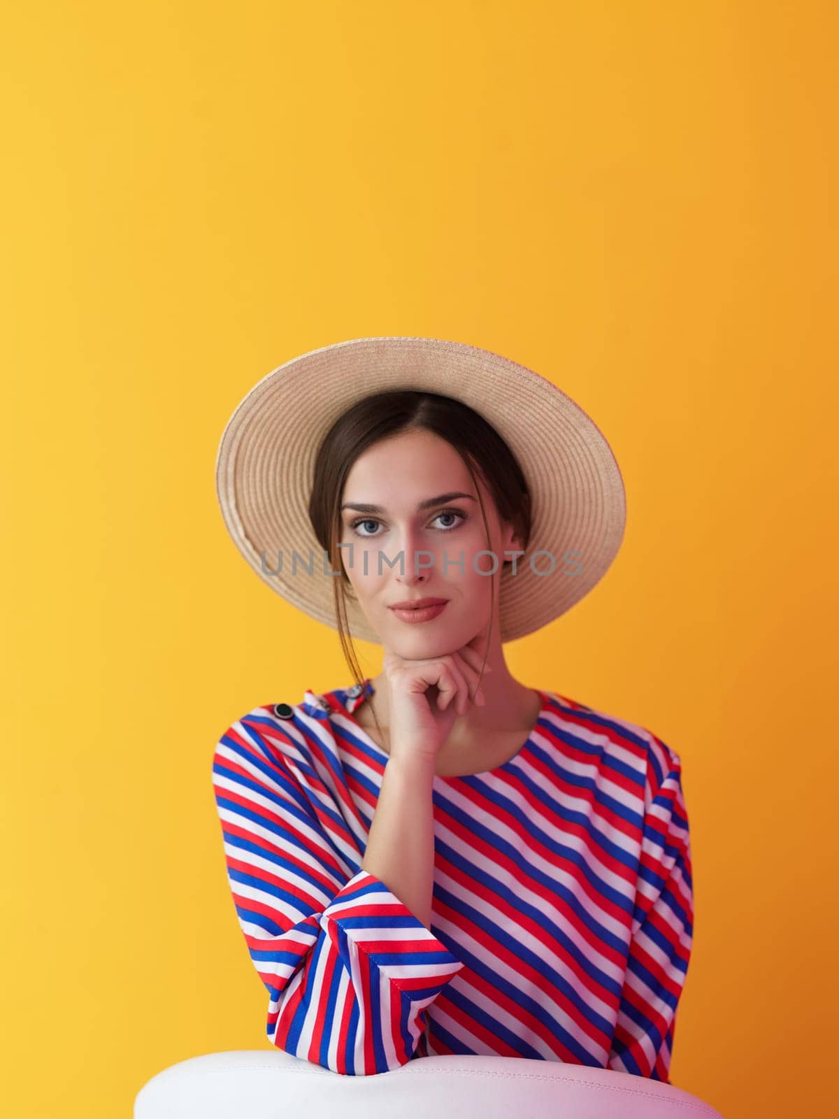 Portrait of young woman sitting on the chair isolated on yellow background. Female model in casual and modern clothes posing in the studio