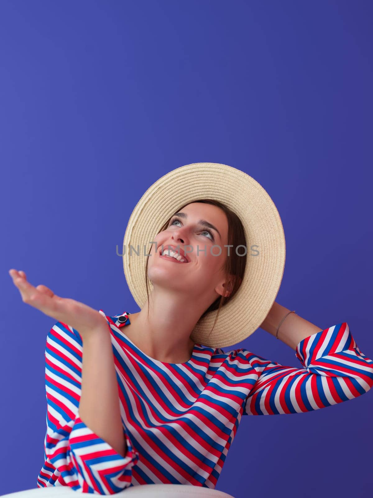 Portrait of young woman sitting on the chair isolated on purple background. Female model in casual and modern clothes posing in the studio