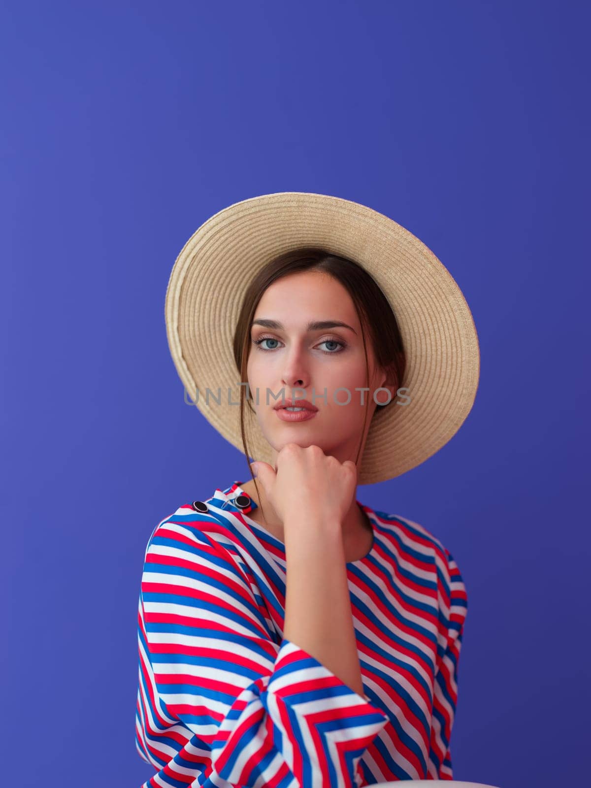 Portrait of young woman sitting on the chair isolated on purple background. Female model in casual and modern clothes posing in the studio