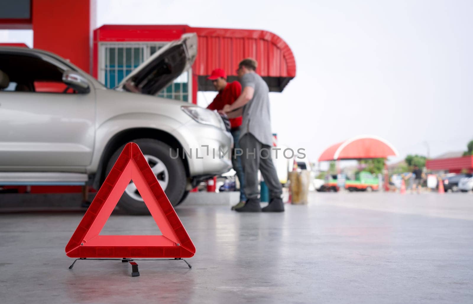 Red triangle reflector roadside warning on the floor. There is a broken pickup car in the background.
