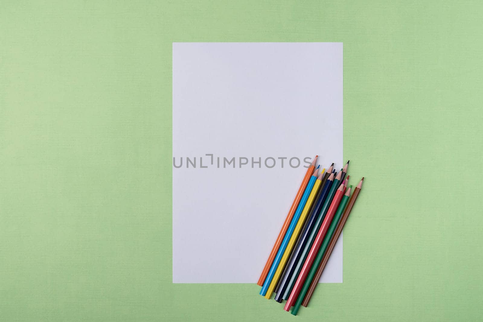 A blank white sheet and colored pencils for drawing on a plain textured background with space for copying and lettering. Layout, mockup free space.