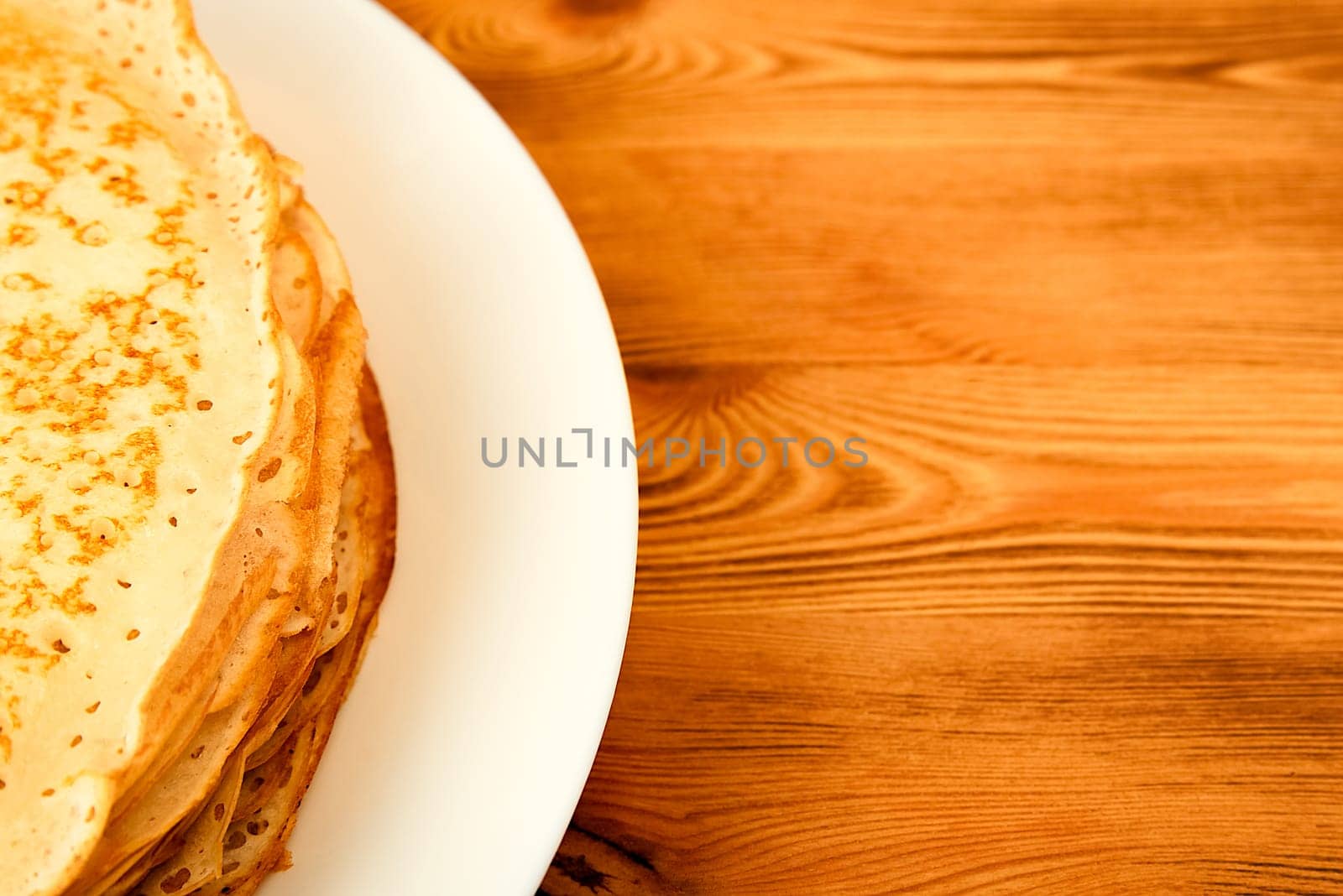 Pancakes on a plate on a wooden table. A large stack of fresh pancakes. Delicious healthy fresh pancakes. Place for advertising, logo, lettering, layout, mockup.