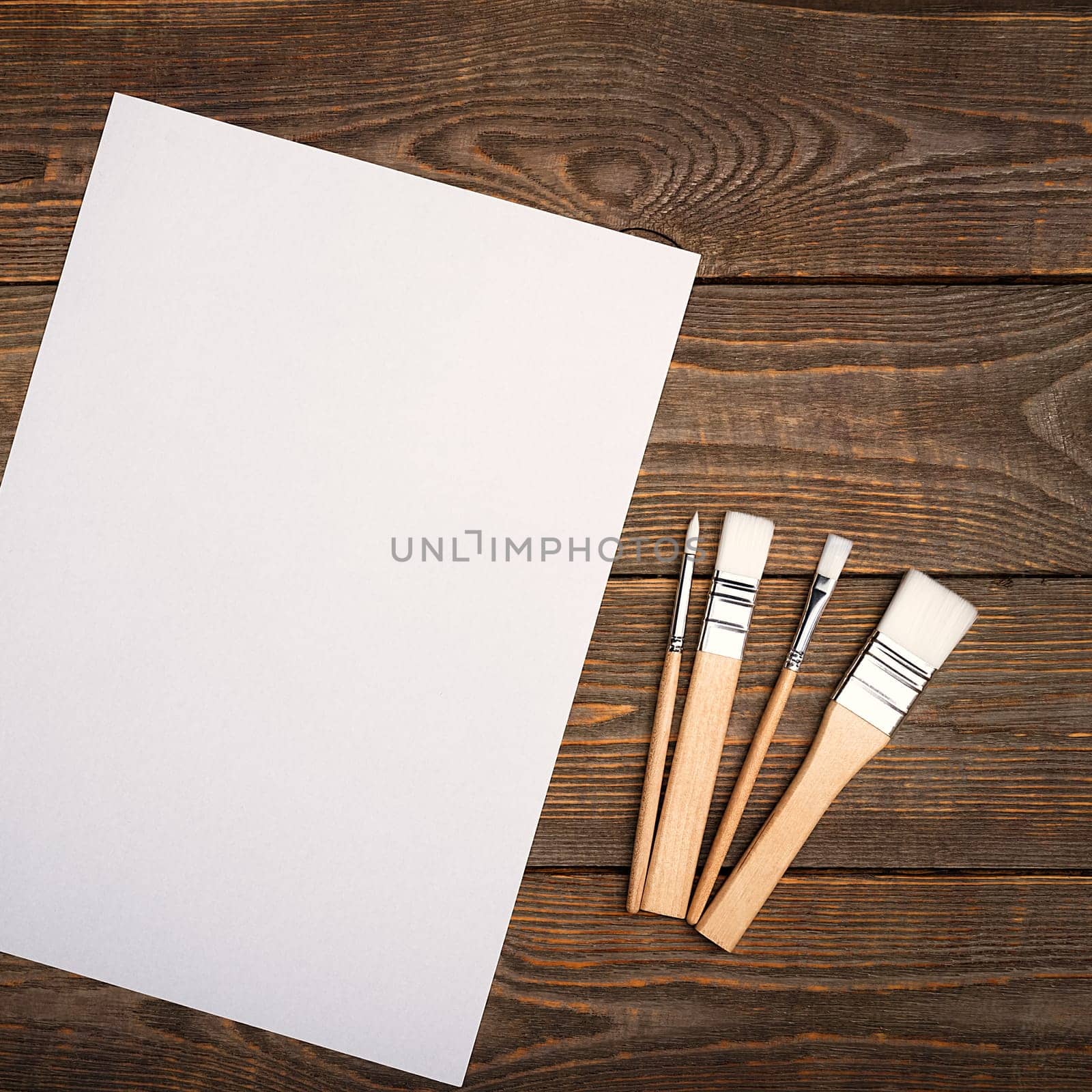 A clean white sheet and brushes on a textured background with space to copy. Layout, mockup space for text and drawing.