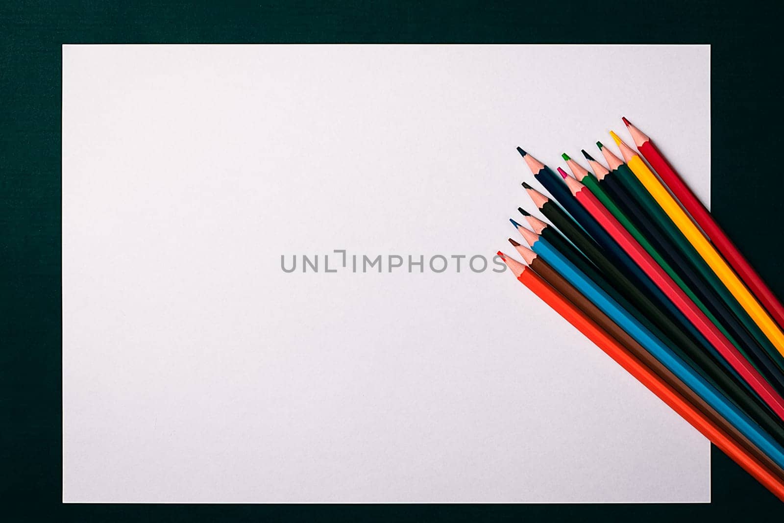A blank white sheet and colored pencils for drawing on a plain textured background with space for copying and lettering. Layout, mockup free space.