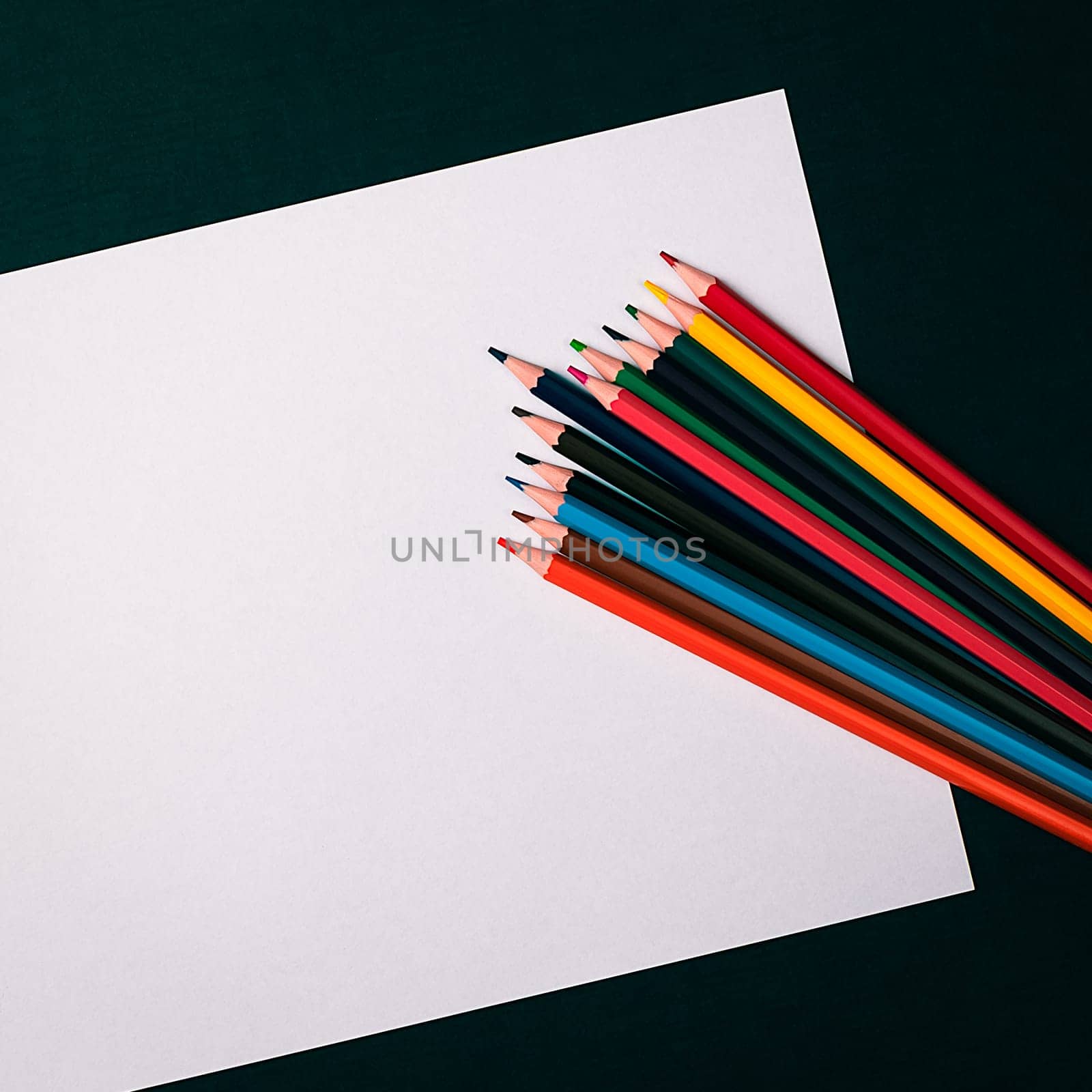 A blank white sheet and colored pencils for drawing on a plain textured background with space for copying and lettering. Layout, mockup free space.