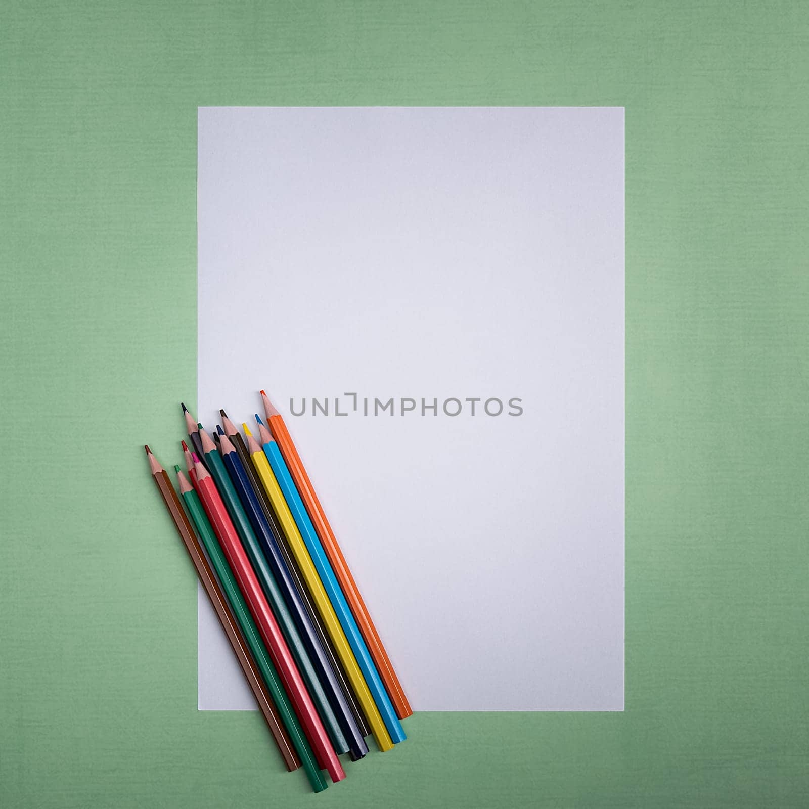 A blank white sheet and colored pencils for drawing on a plain textured background with space for copying and lettering. Layout, mockup free space.