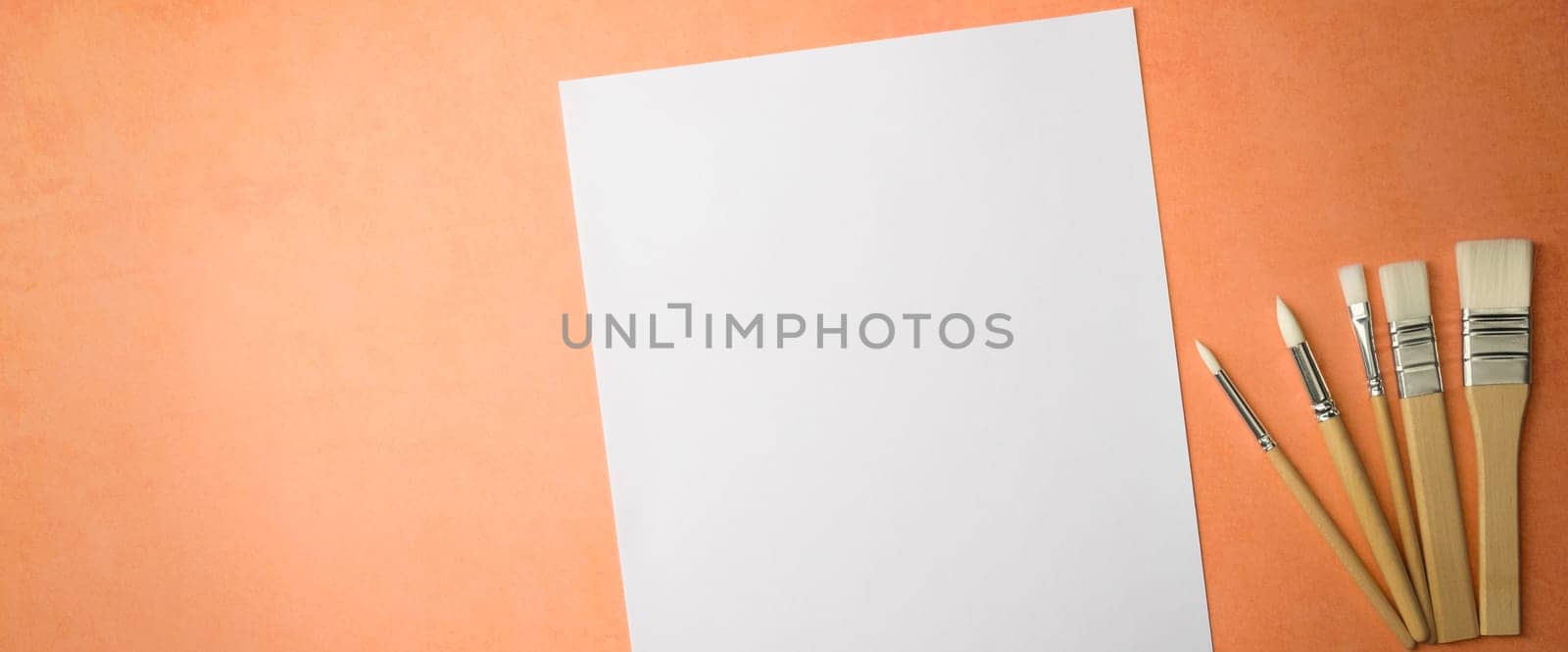 A clean white sheet and brushes on a textured background with space to copy. Layout, mockup space for text and drawing.