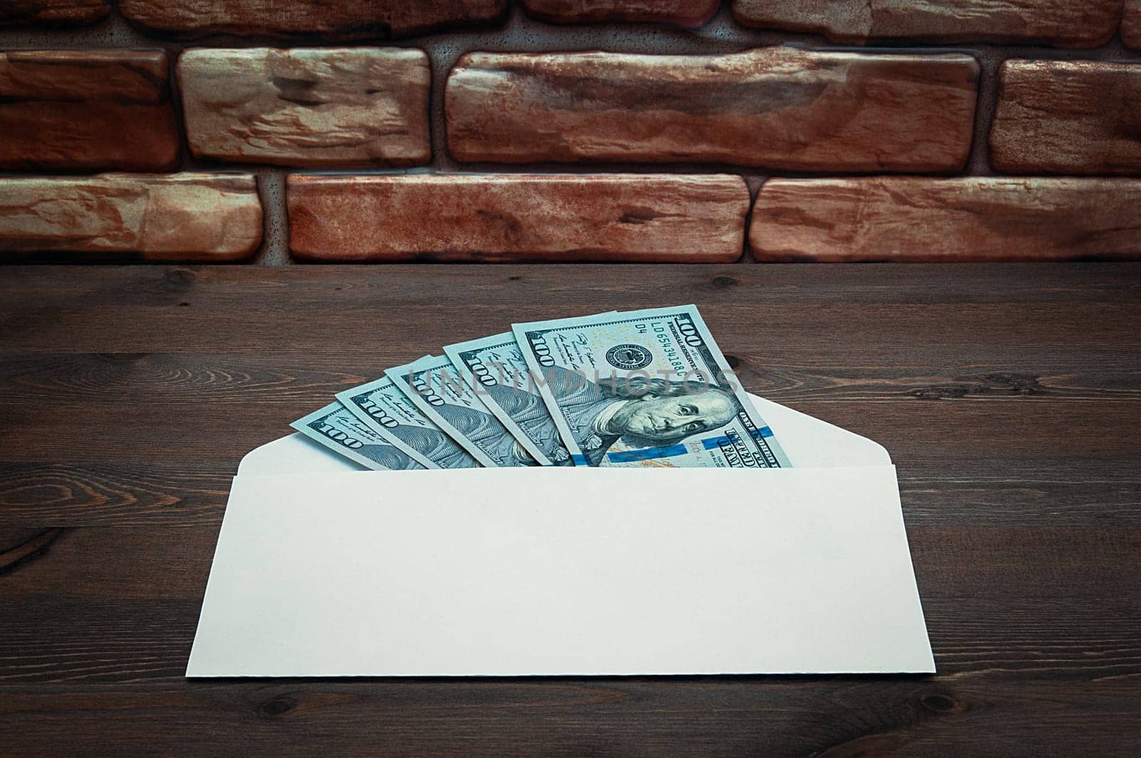 Dollars in one-hundred-dollar bills are spread out in an envelope on a table near the brick wall. Dollars fanned out. US dollars. On the envelope there is a place for an inscription, a logo. Color style. Layout, template, mockup.
