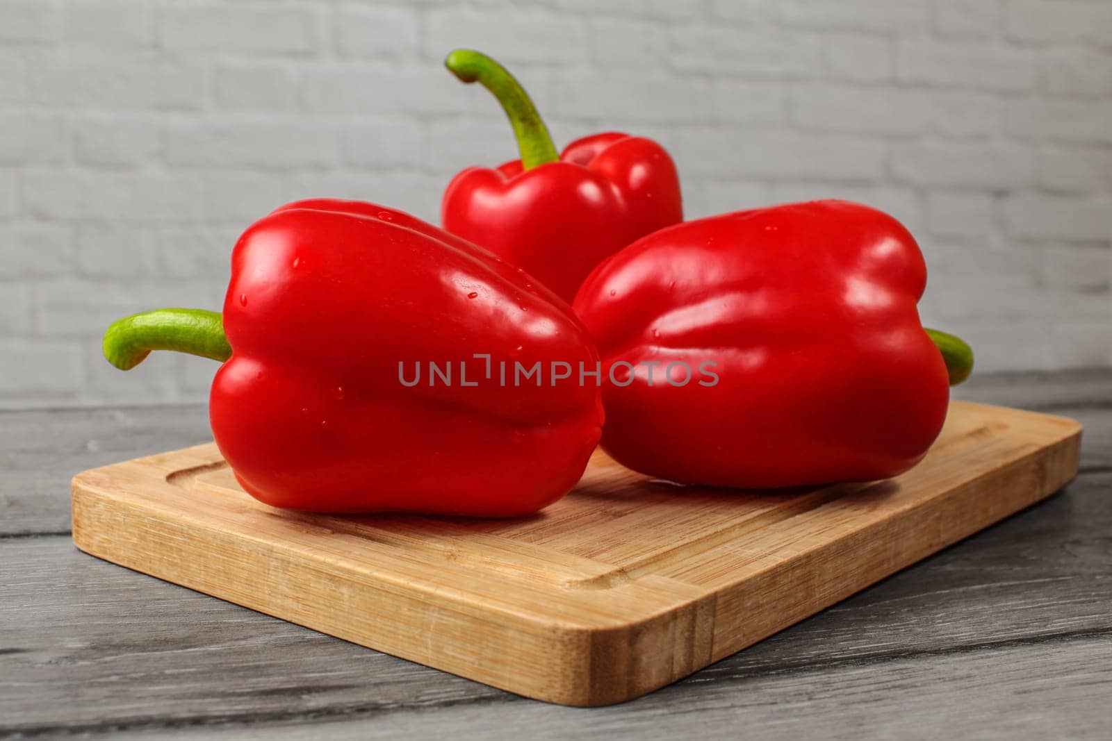 Three bright red bell peppers on old wooden cutting board.
