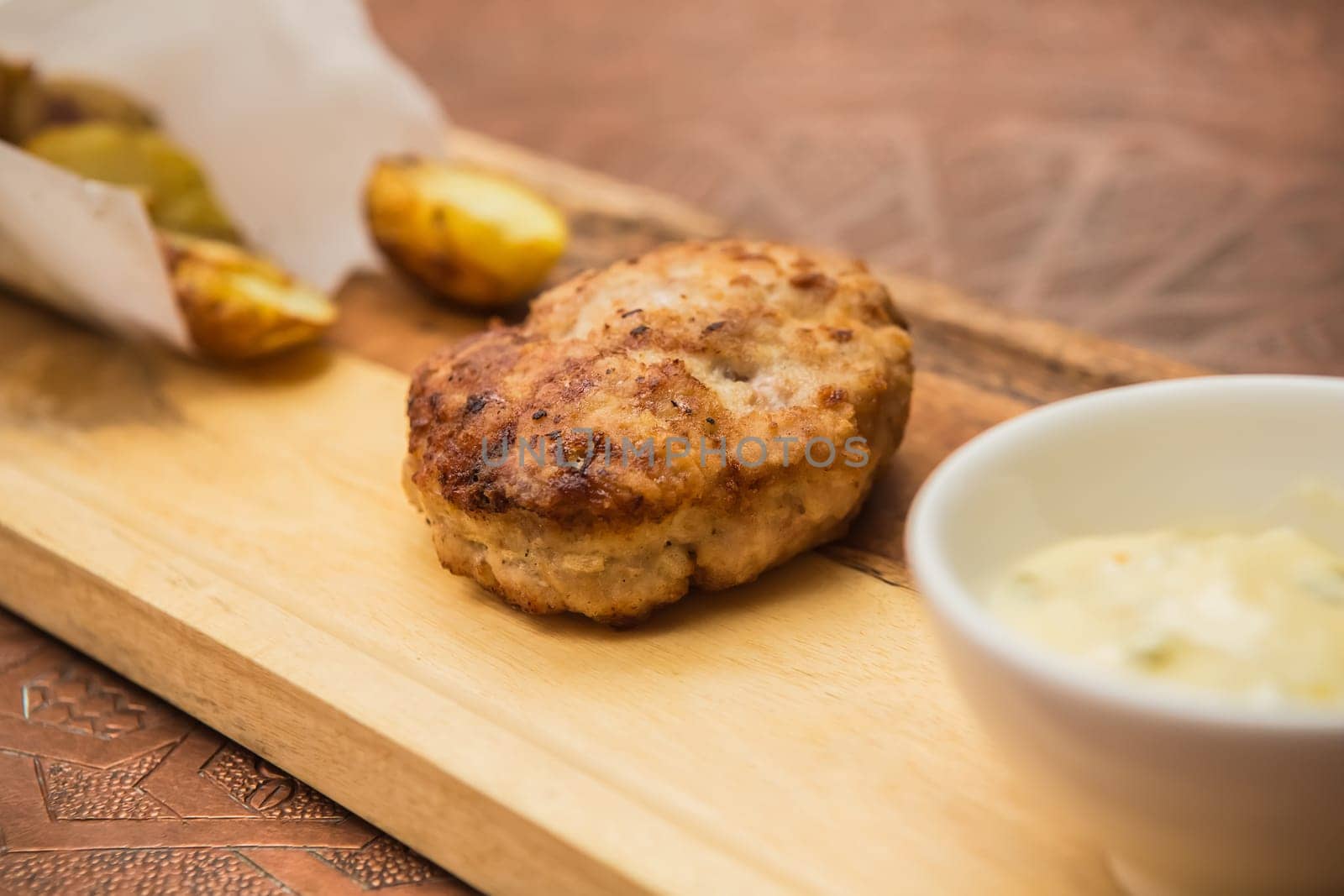 Succulent cooked beef burger with potato on a wood plate.