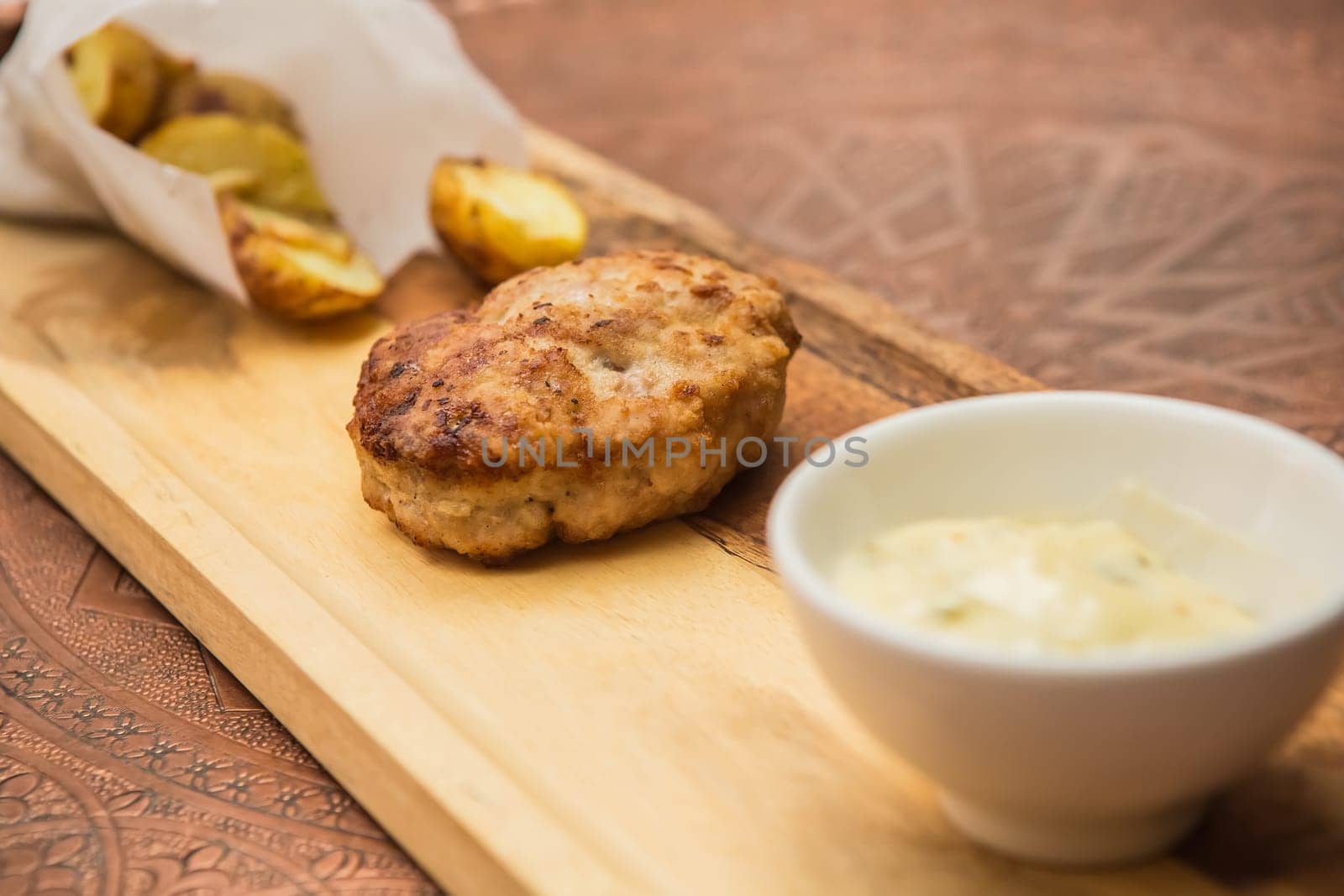Succulent cooked beef burger with potato on a wood plate.