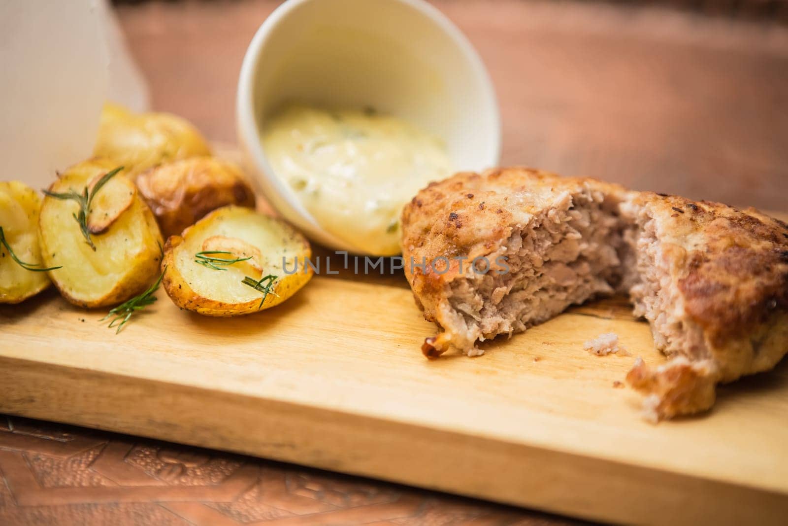 Succulent cooked beef burger with potato on a wood plate.