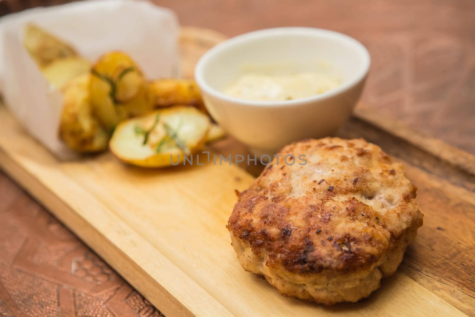 Succulent cooked beef burger with potato on a wood plate.