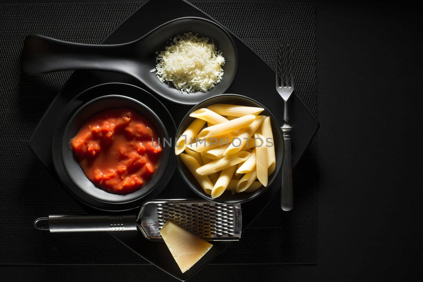 Penne pasta with tomatoes sauce and parmesan on black background