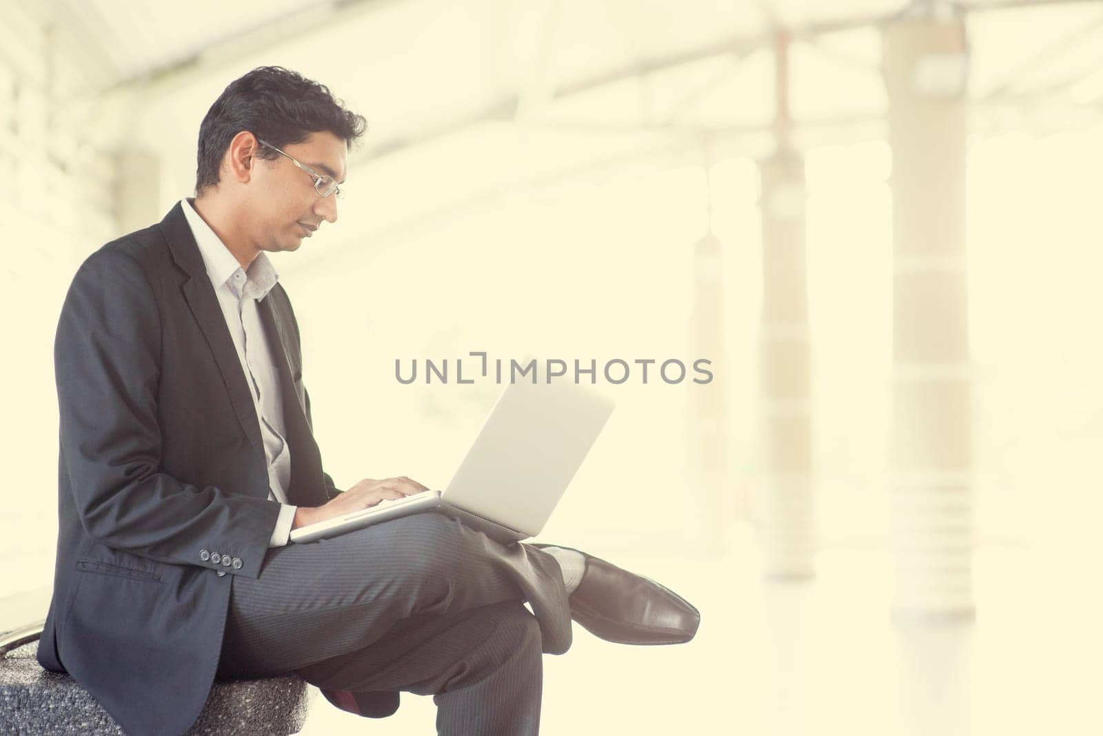 Asian Indian businessman using laptop computer while waiting train at railway station.