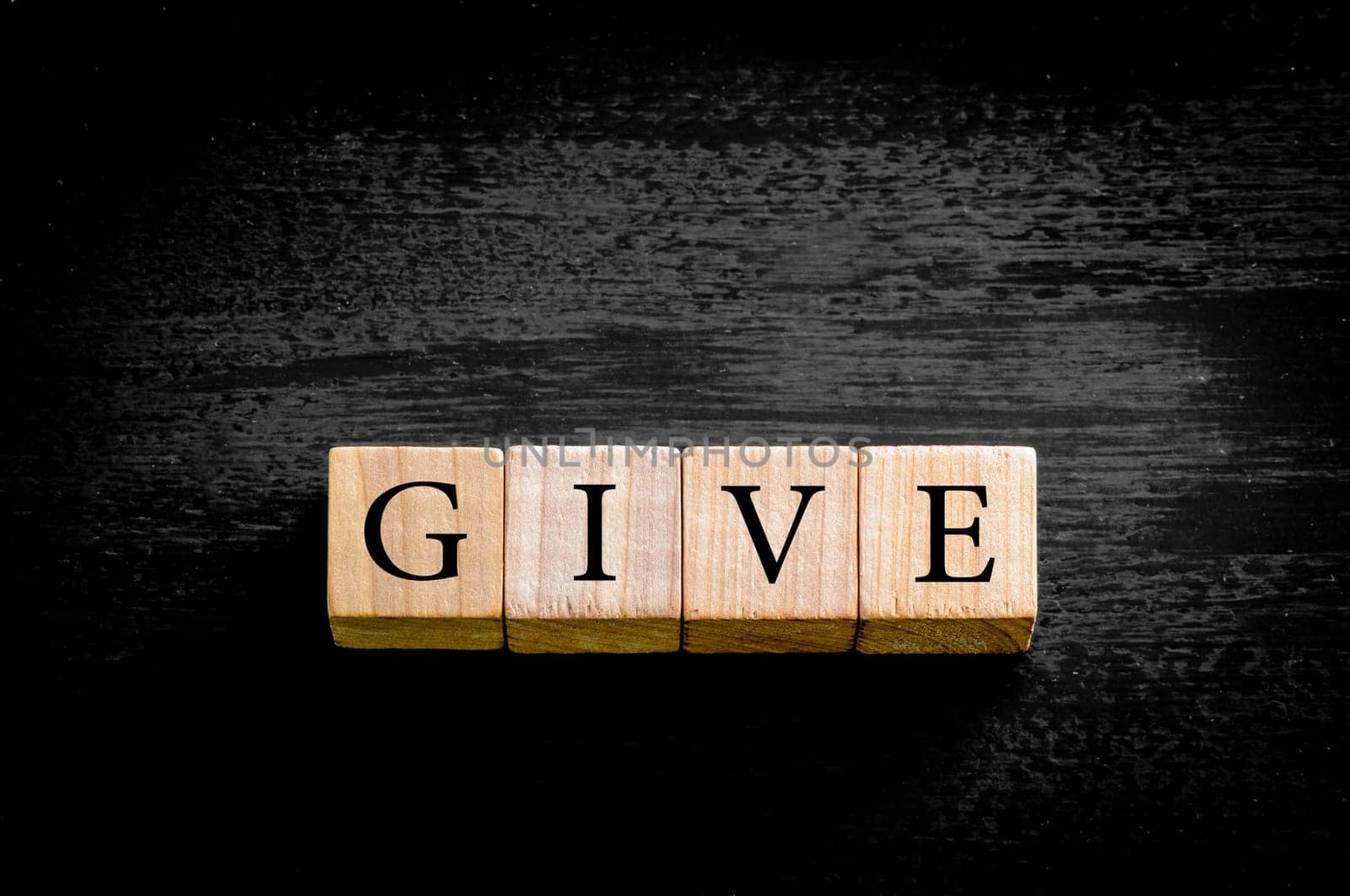 Word GIVE. Wooden small cubes with letters isolated on black background with copy space available. Concept image.