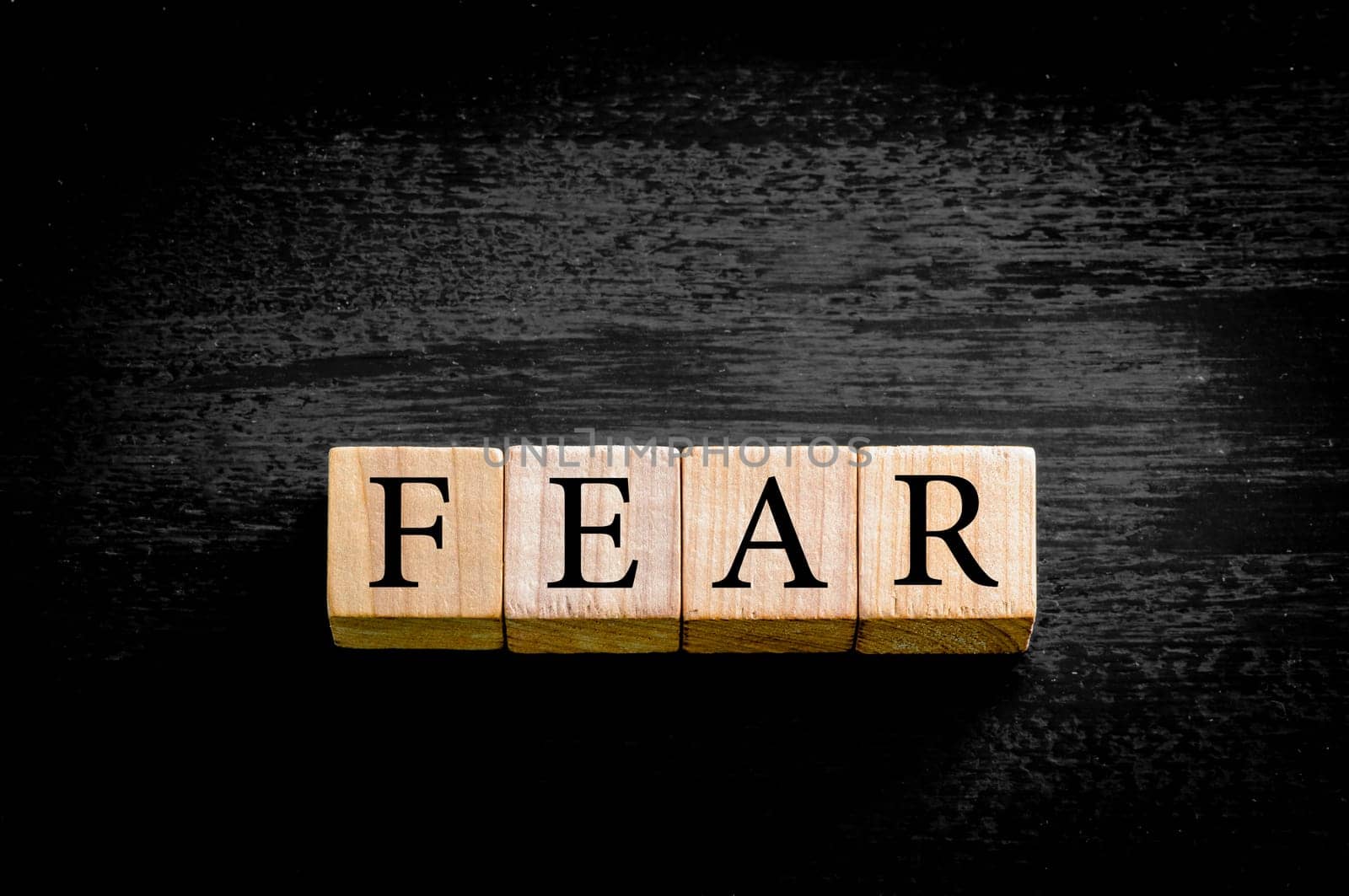 Word FEAR. Wooden small cubes with letters isolated on black background with copy space available. Concept image.