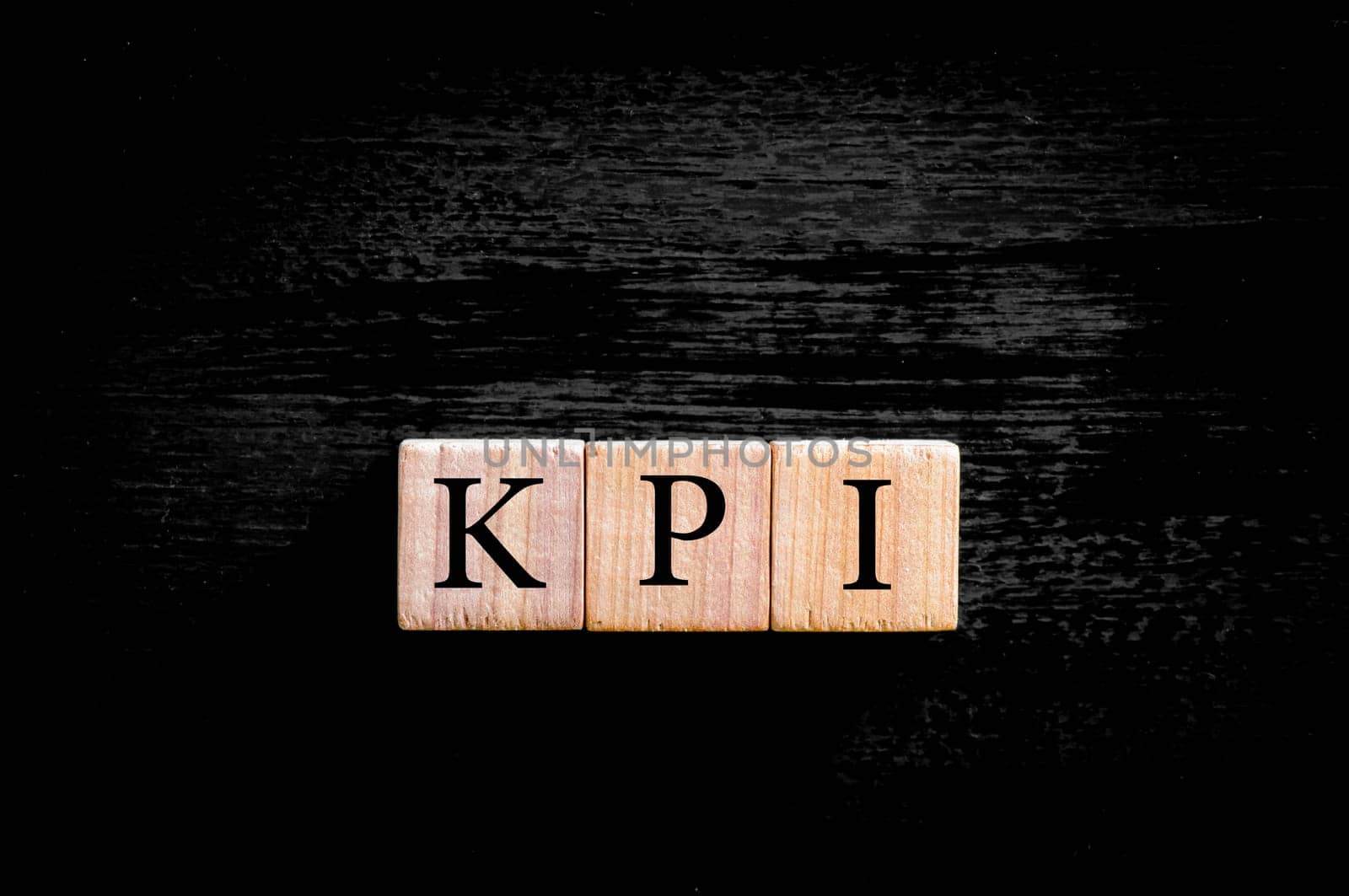 Acronym KPI - key performance indicator. Wooden small cubes with letters isolated on black background with copy space available. Business Concept image.