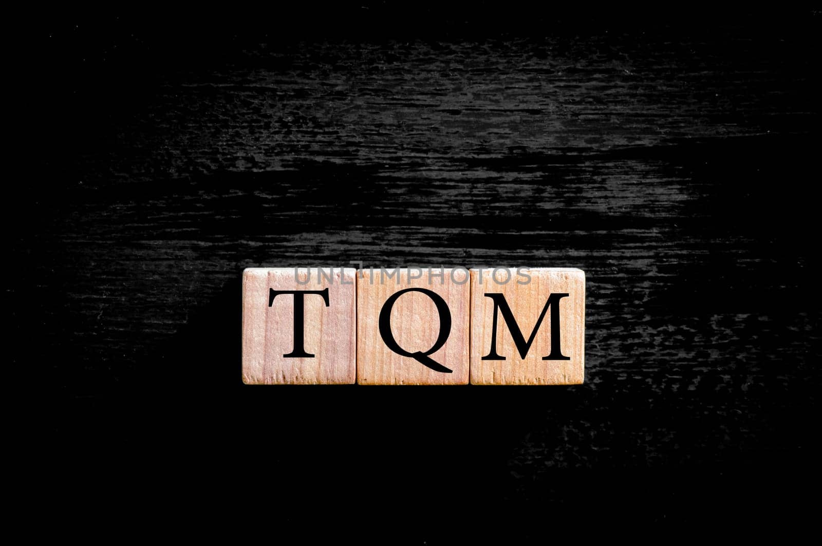 Acronym TQM - Total Quality Management. Wooden small cubes with letters isolated on black background with copy space available.Business Concept image.