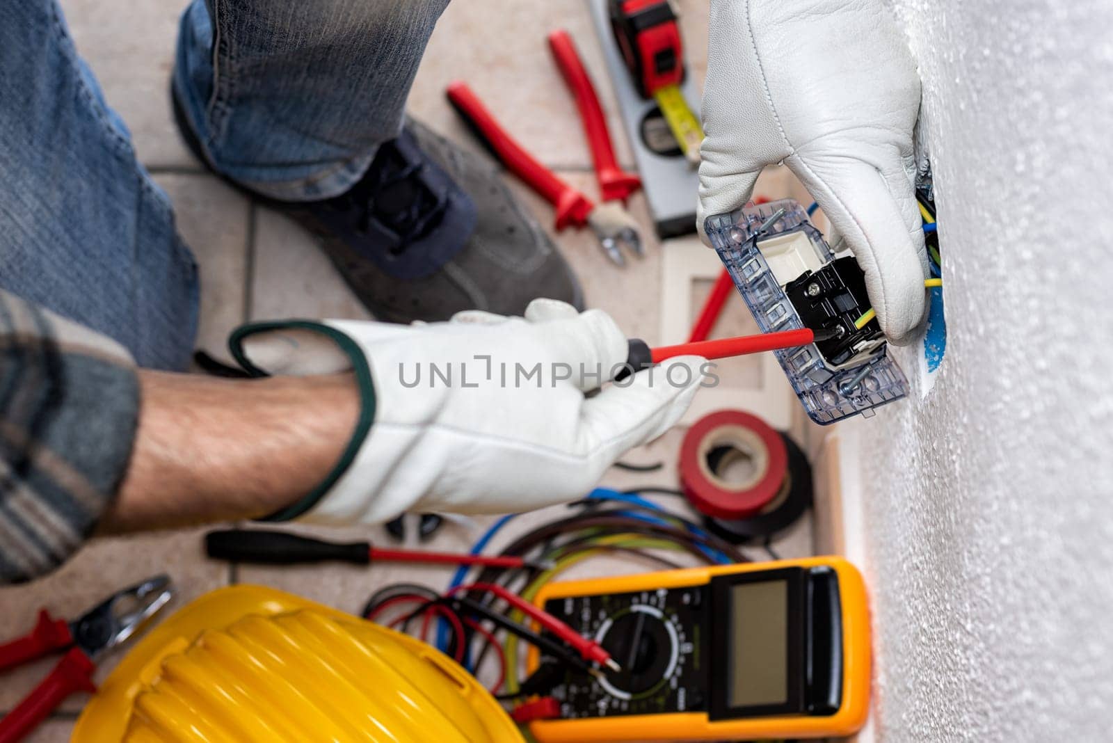 View from top. Electrician worker with screwdriver fixes electrical cables in the terminals of the socket of an electrical system. Working safely with protective gloves. Construction industry.