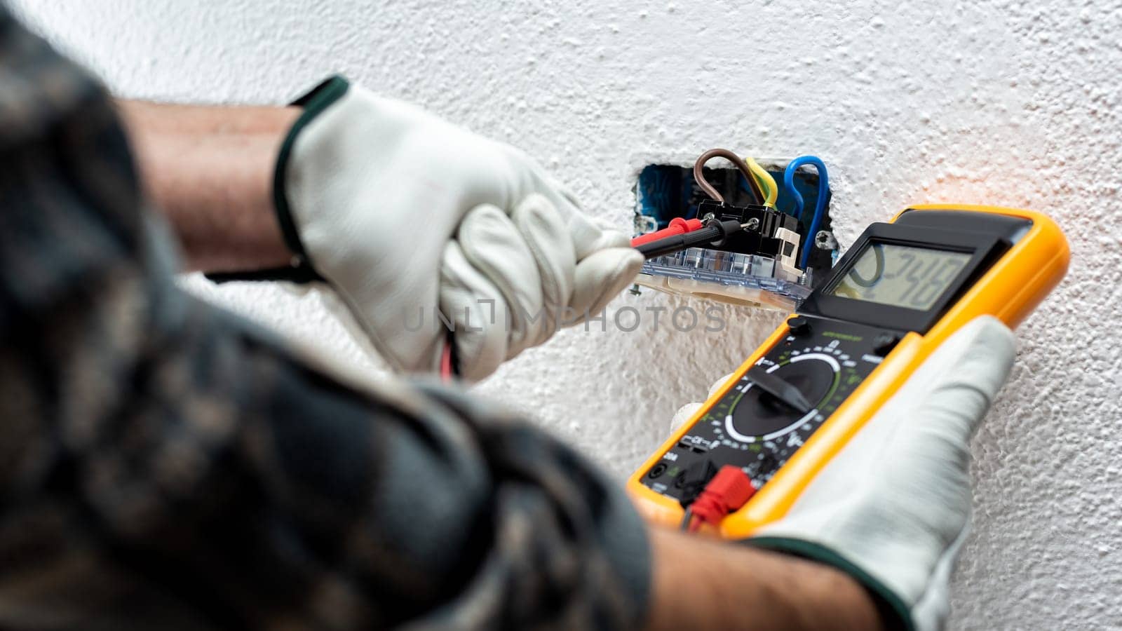 Electrician worker at work with the tester measures the voltage in an electrical system. Working safely with protective gloves. Construction industry.