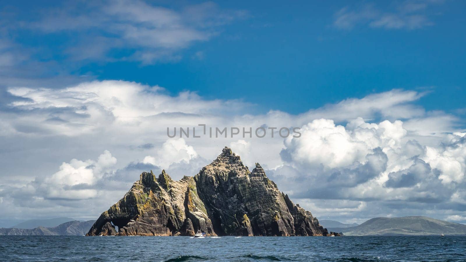 Cruise boat in front of Little Skellig island, habitat of Gannets, Morus Bassanus, with Irish coastline in the background, Ring of Kerry, Ireland
