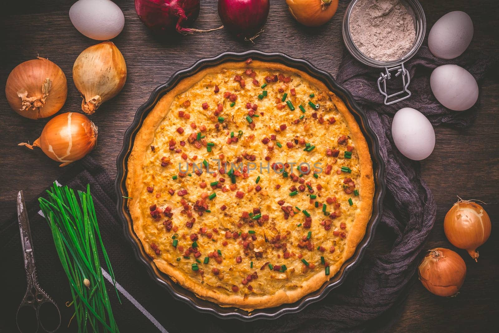 Homemade onion tart or pie with bacon and chives on wooden background