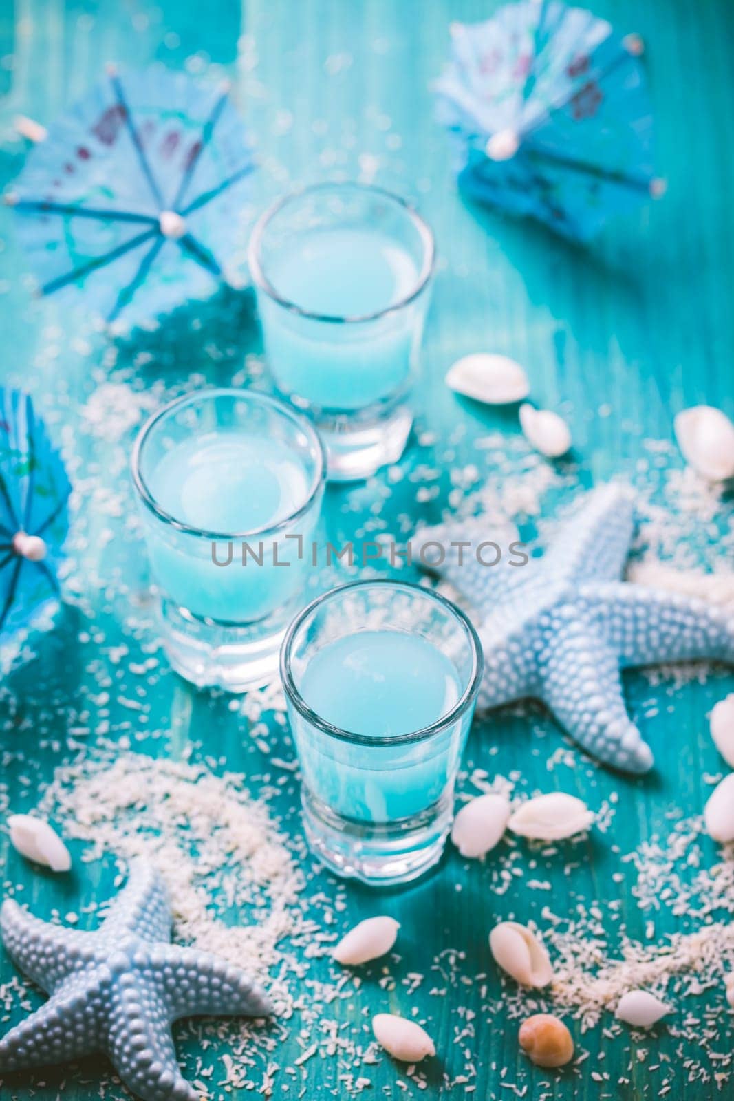 Blue shots for summer with seashells on blue background. Small alcoholic cocktails.