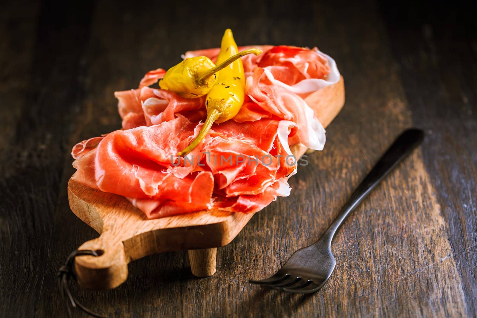 Prosciutto with grilled peppers - Italian dry ham with grilled green peppers on wooden table