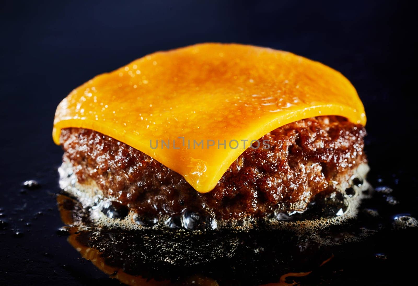 Tasty cheeseburger with beef patty sizzling on a grill in a close up on the melted cheese and juicy meat over a dark background for menu advertising